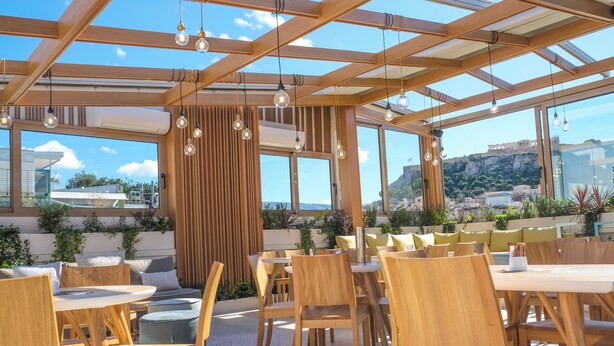 An outdoor dining area with wooden furniture and large windows overlooking a cityscape.
