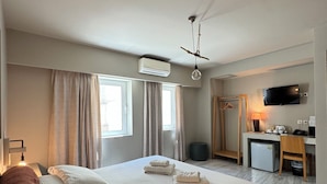 A hotel room with a large bed, a desk with a chair, a television, and an air conditioning unit.