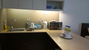 A compact kitchen with a sink, a microwave, and a small countertop. There are bottles of water and a plate with food on the counter. - AL-Aidid Homestay (Kota Bharu)