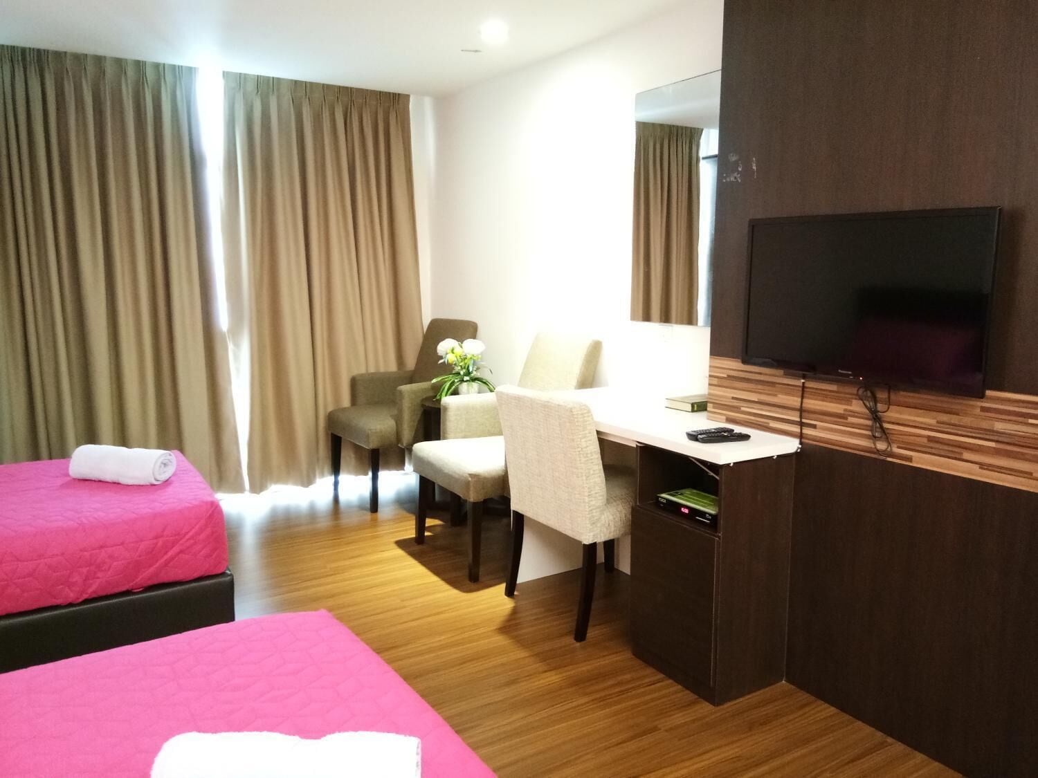 A hotel room with two beds, a desk, a chair, a TV, and a window with curtains.