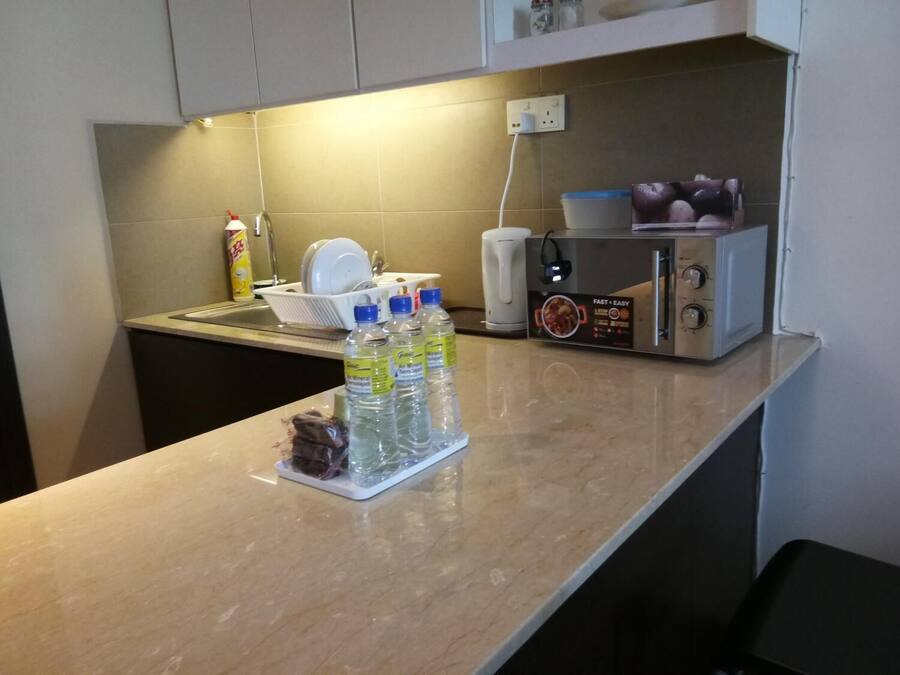 A kitchen with a microwave, a kettle, and a dish rack. There are bottled water and a dish soap bottle on the counter.