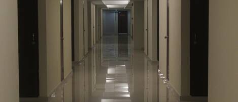 A long, narrow hotel corridor with doors on both sides and a tiled floor.
