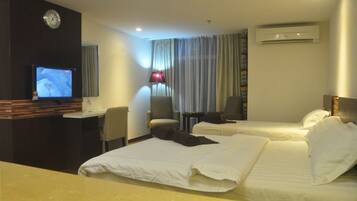 A hotel room with a bed, a desk with a television, a chair, and an air conditioning unit.