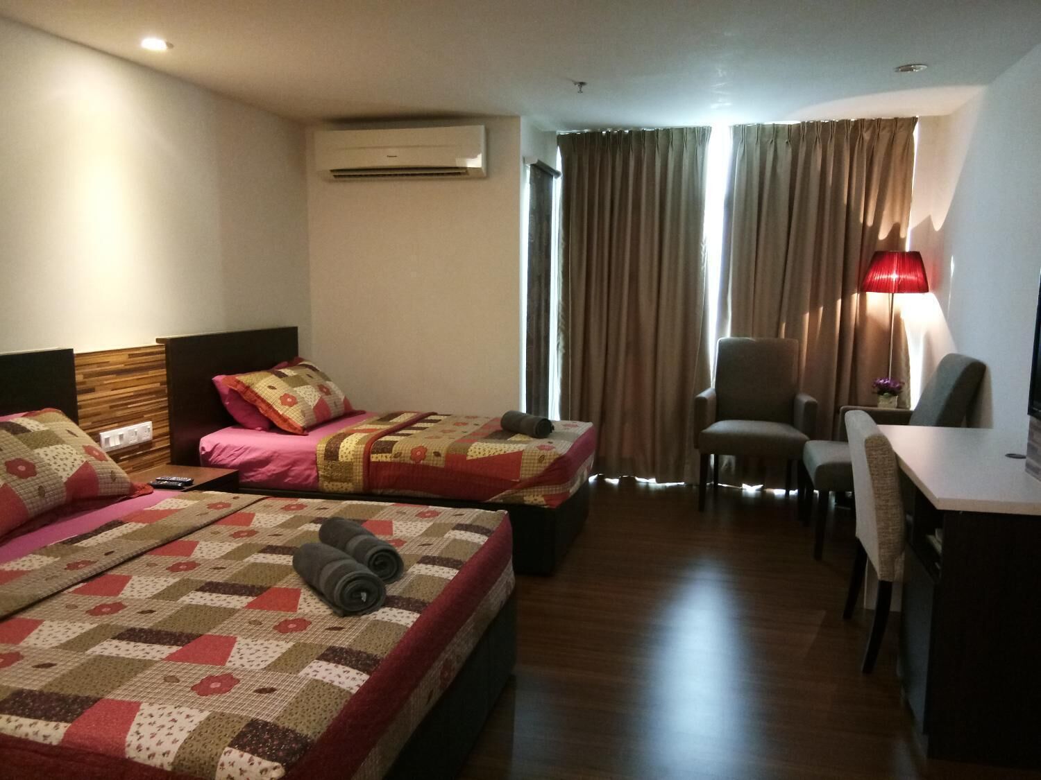 A hotel room with two beds, a desk, a chair, an air conditioning unit, and a window with curtains.
