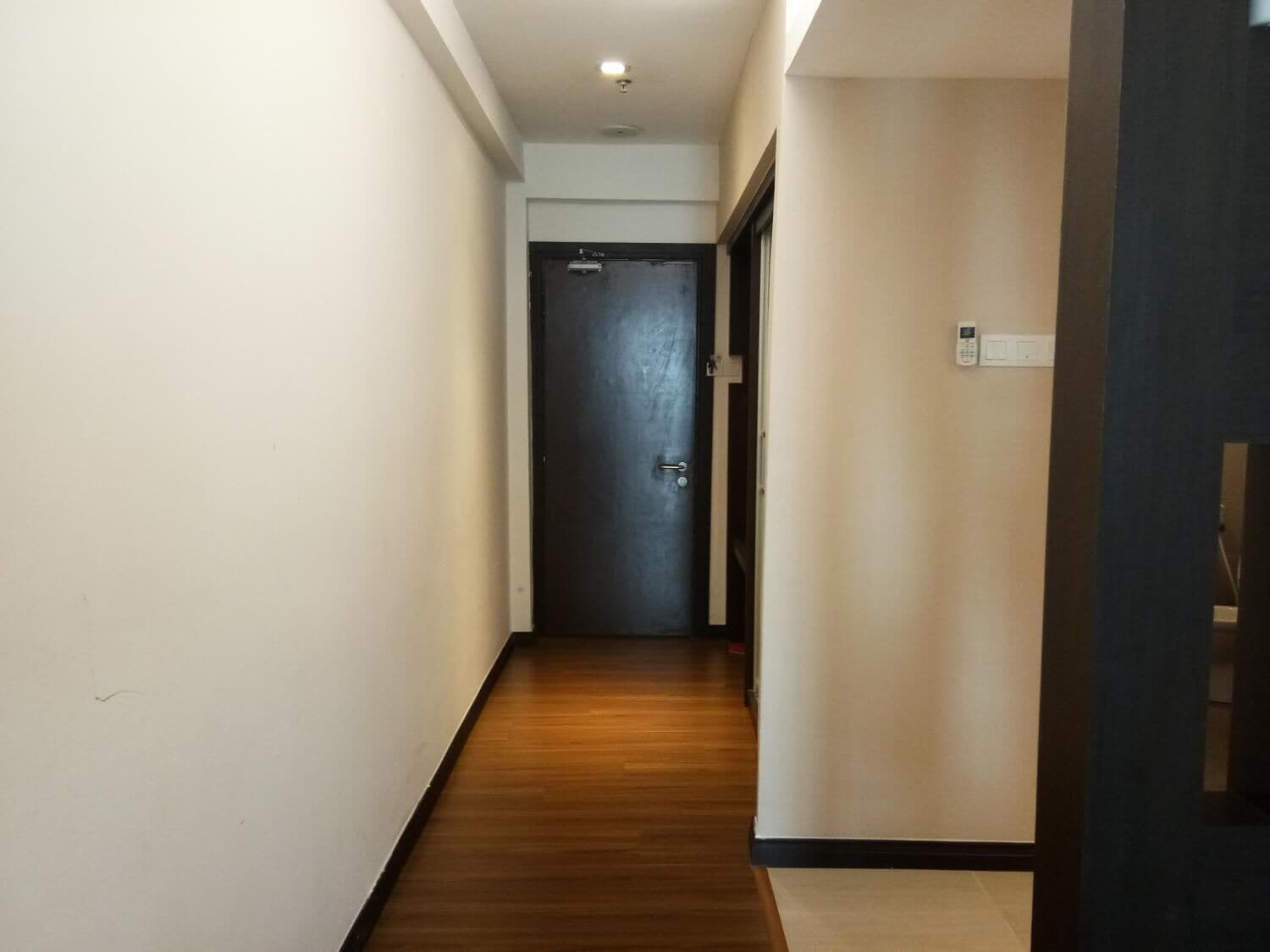 A narrow hallway with wooden flooring, a dark door at the end, and a light switch on the wall.