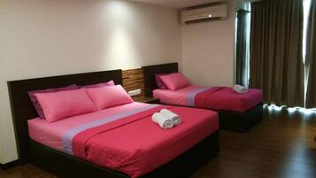 A hotel room with two beds, each with pink bedding and a wooden headboard. There is an air conditioning unit on the wall, and a window with curtains.