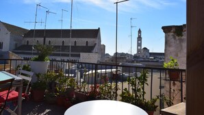 A rooftop terrace with potted plants, a table, and chairs. In the background, there is a building with a clock tower. - Il Trespolo degli Angeli (Bari)