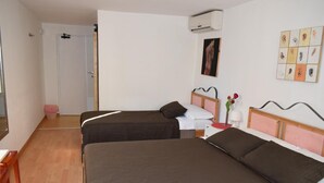 A hotel room with two single beds, a wooden floor, a white door, and a wall-mounted air conditioner. - Il Trespolo degli Angeli (Bari)