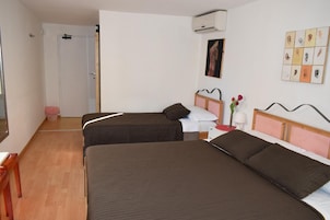 Habitación de hotel con dos camas individuales, piso de madera, puerta blanca y aire acondicionado instalado en la pared.
