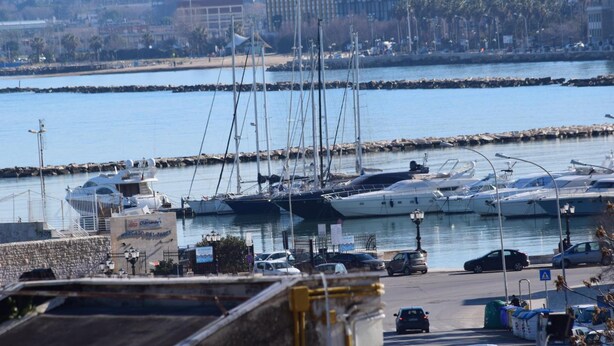 A marina with multiple yachts docked, a parking area with cars, and a cityscape in the background. - Il Trespolo degli Angeli (Bari)