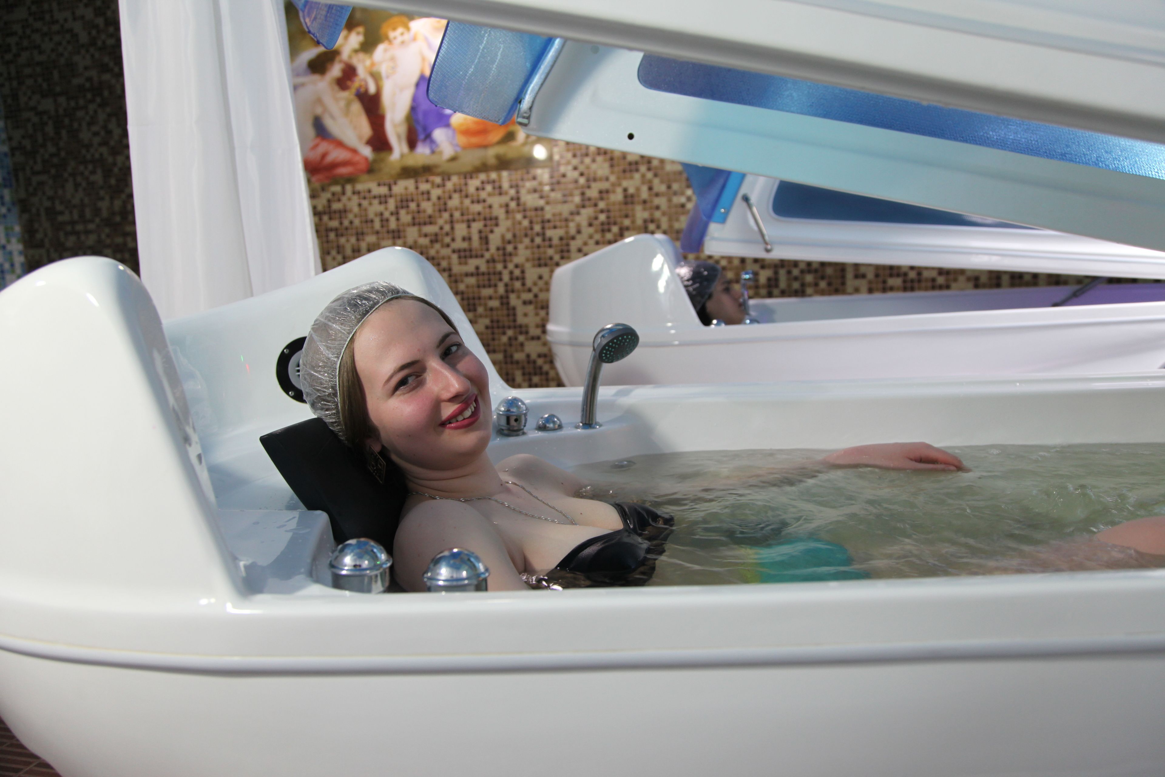 A person in a bathtub with a showerhead and faucets.