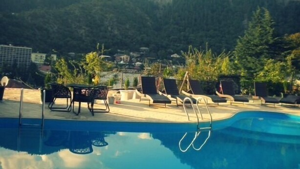 A poolside area with lounge chairs and a pool, surrounded by mountains and greenery. - Borjomi Palace (Borjomi)