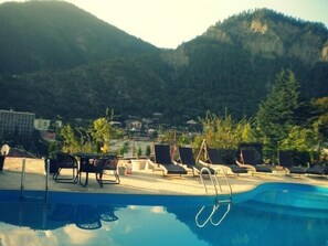 A poolside area with lounge chairs and a pool, surrounded by mountains and greenery. - Borjomi Palace (Borjomi)
