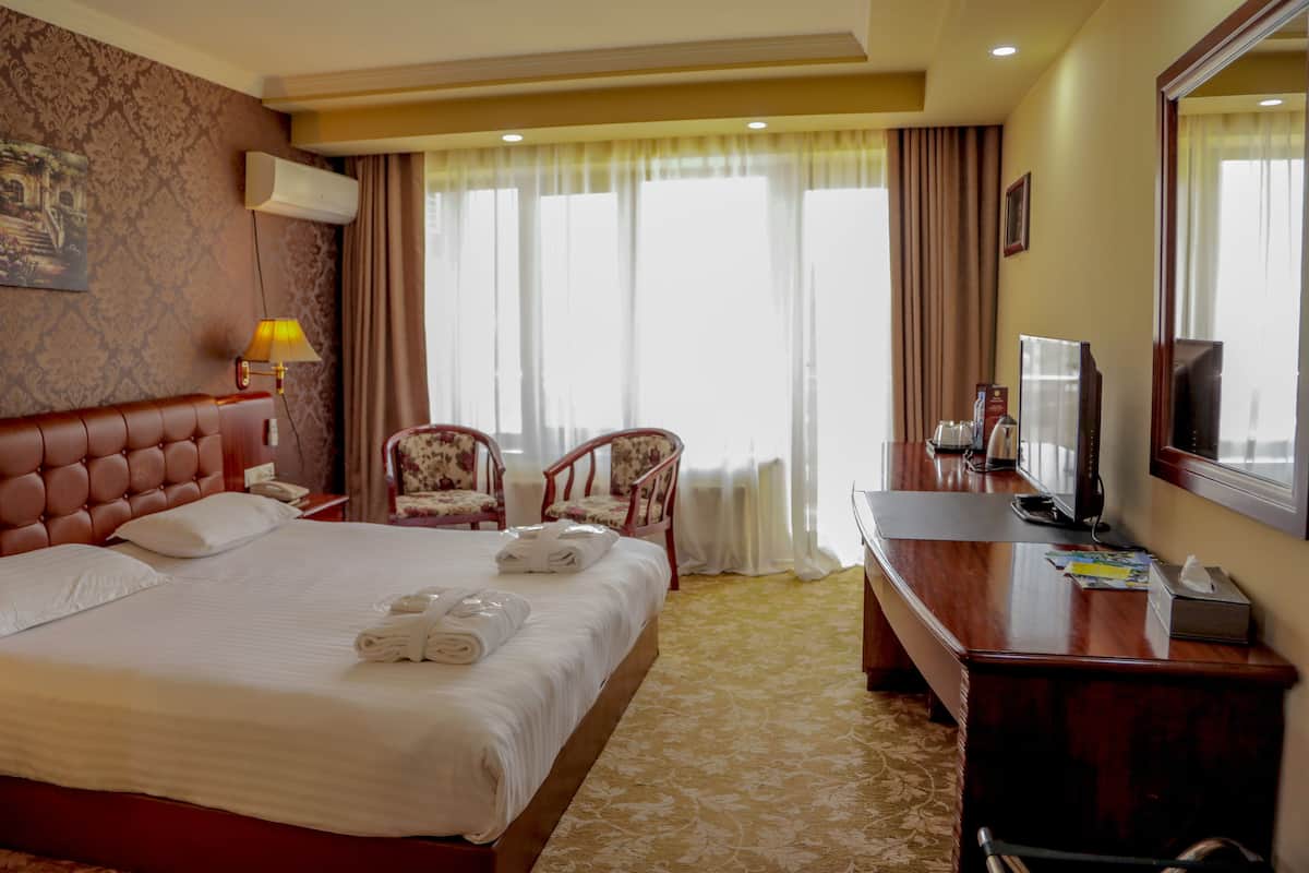 A hotel room with a large bed, two chairs, a desk with a TV, and a mirror.