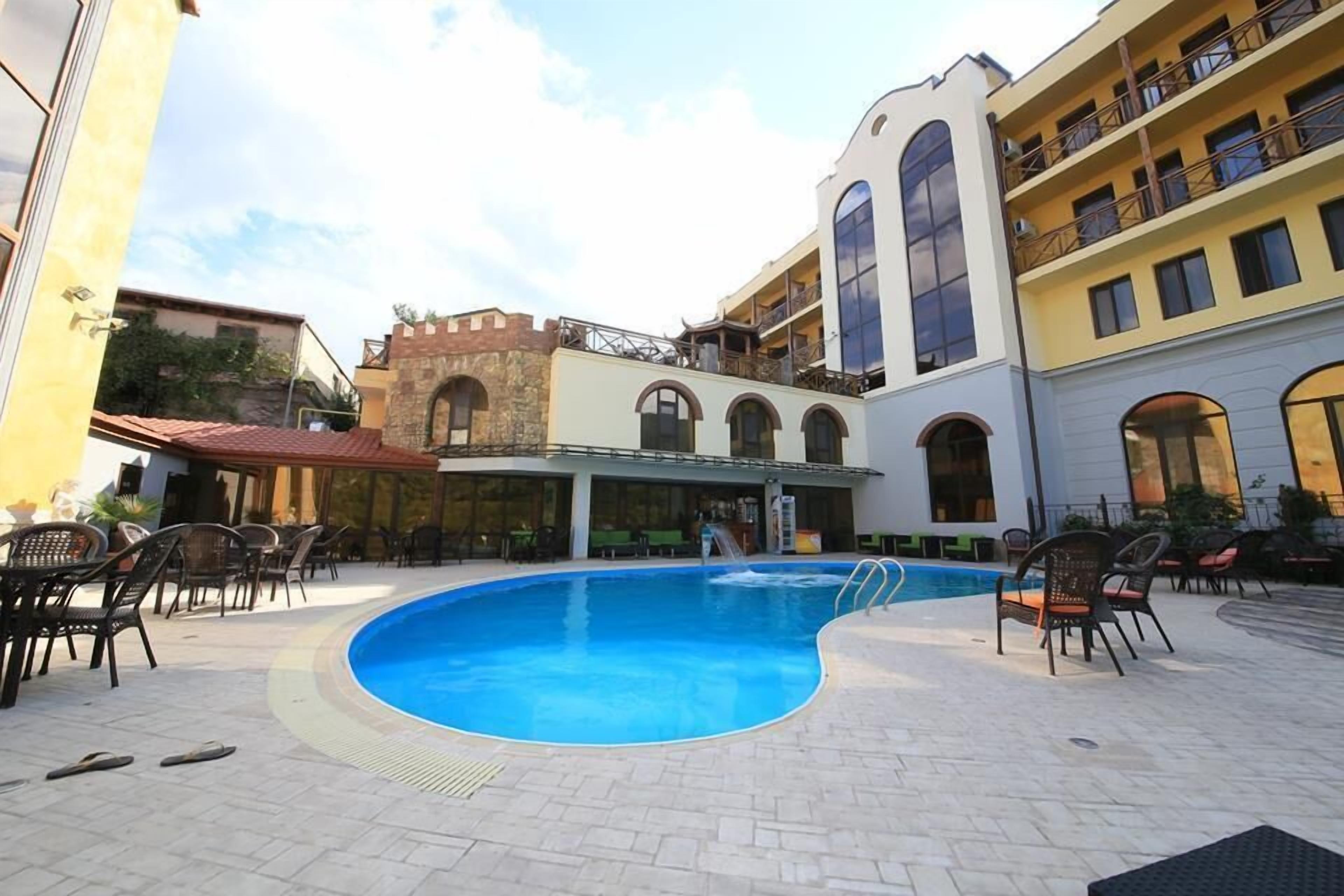 Piscina com espreguiçadeiras e mesas, cercada por edifícios com varandas e janelas em arco.