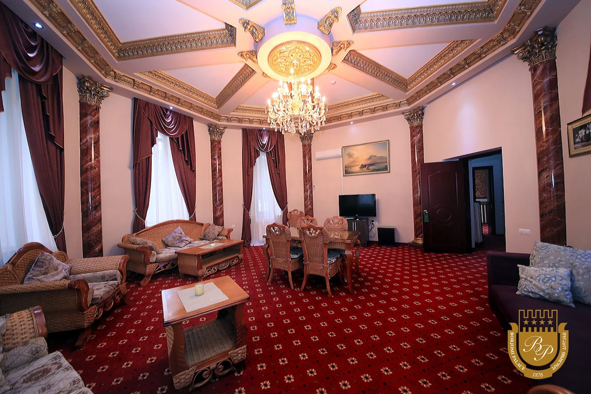 A spacious living room with a red carpet, a chandelier, and a television.
