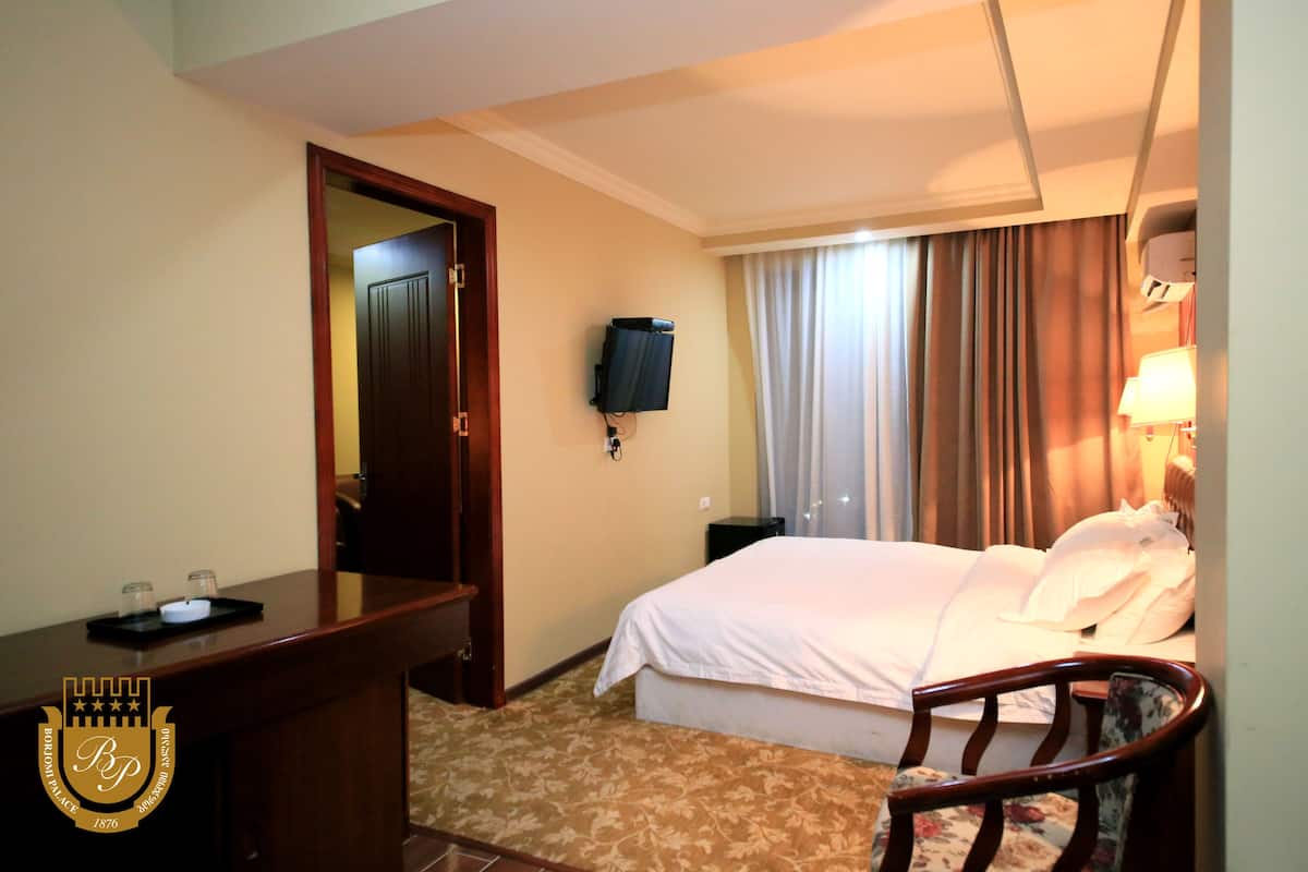 A hotel room with a bed, a desk, a chair, a television, and a window with curtains.