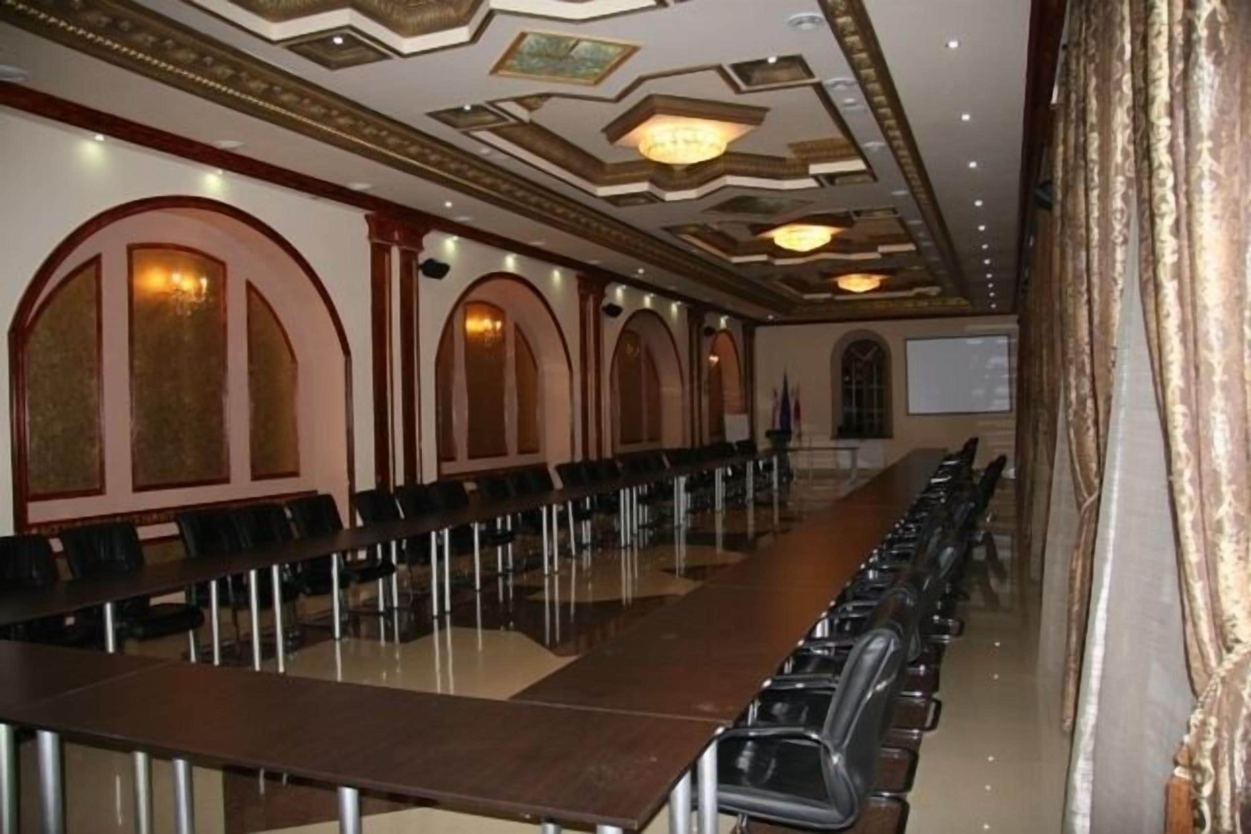 Un salón de conferencias con largas mesas y sillas, diseños de paredes en arco y una pantalla de proyector.