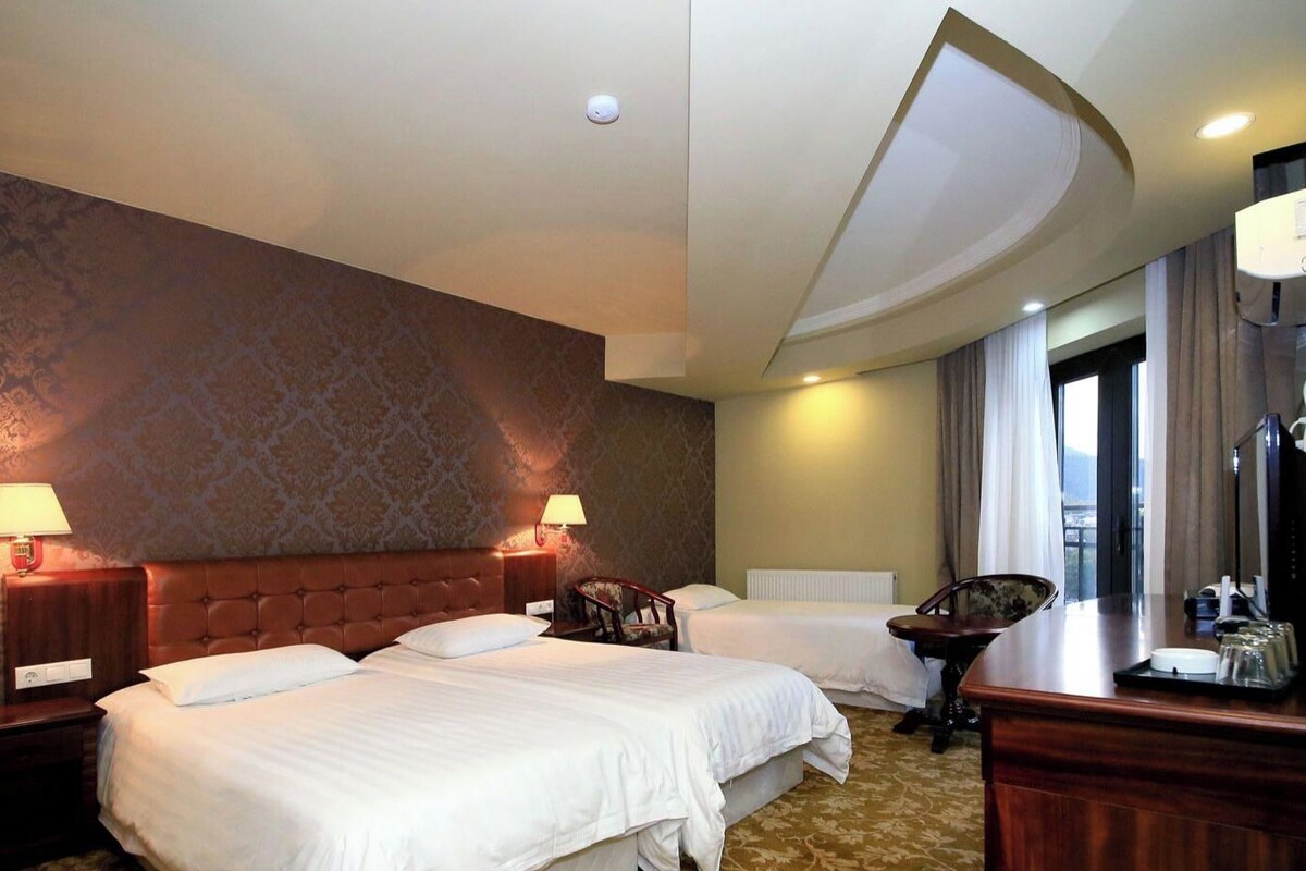 A hotel room with two beds, a desk, a chair, a mirror, and a window with curtains.