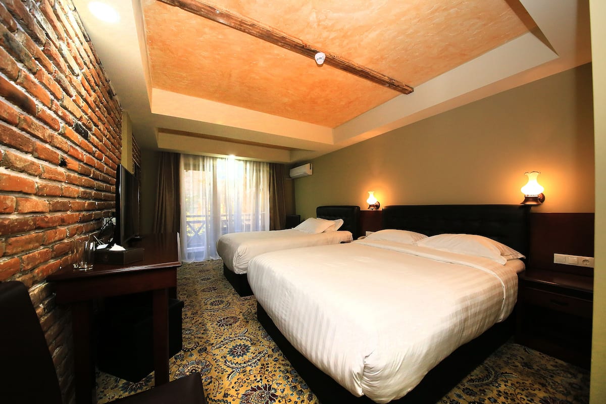 A hotel room with two beds, a brick wall, a ceiling light, and a patterned carpet.