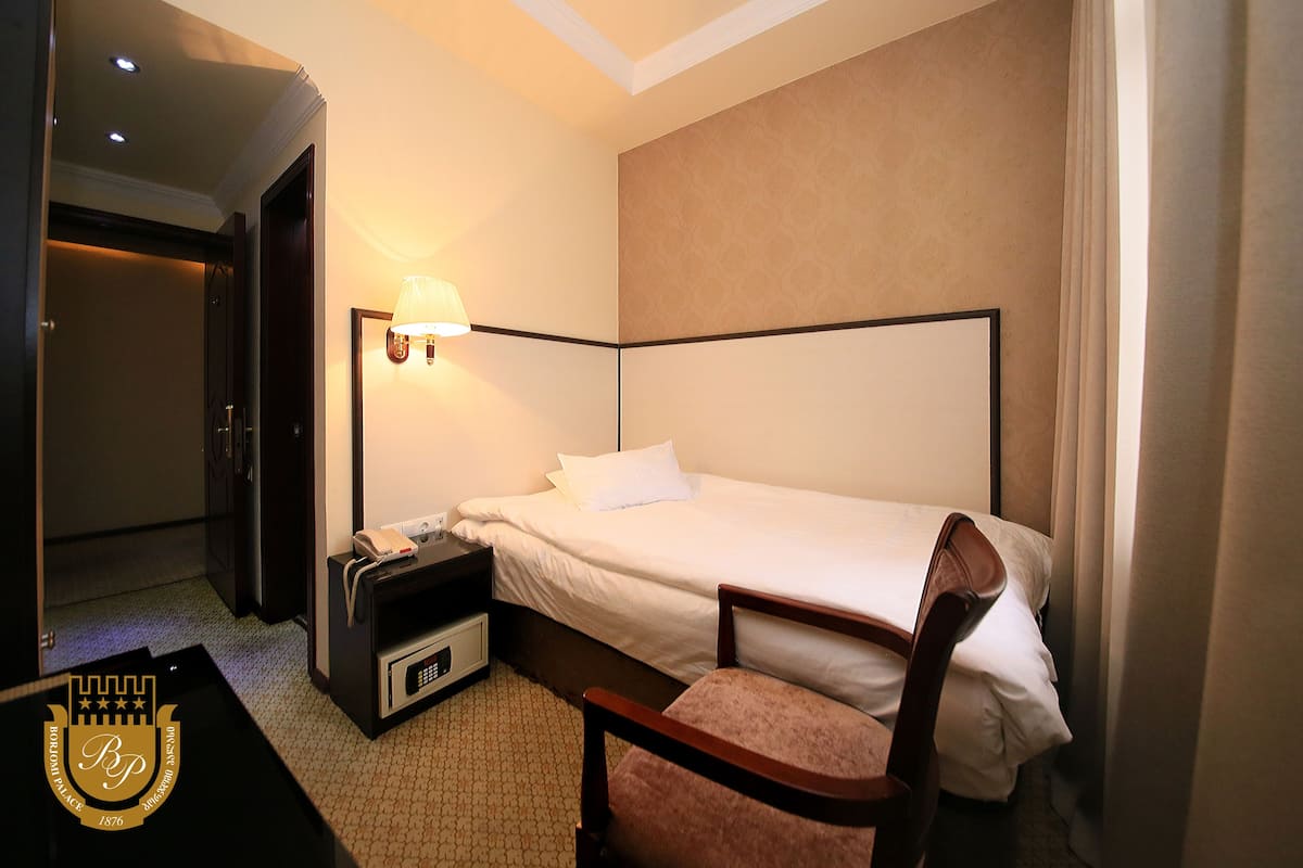 A hotel room with a single bed, a nightstand, a chair, and a lamp.
