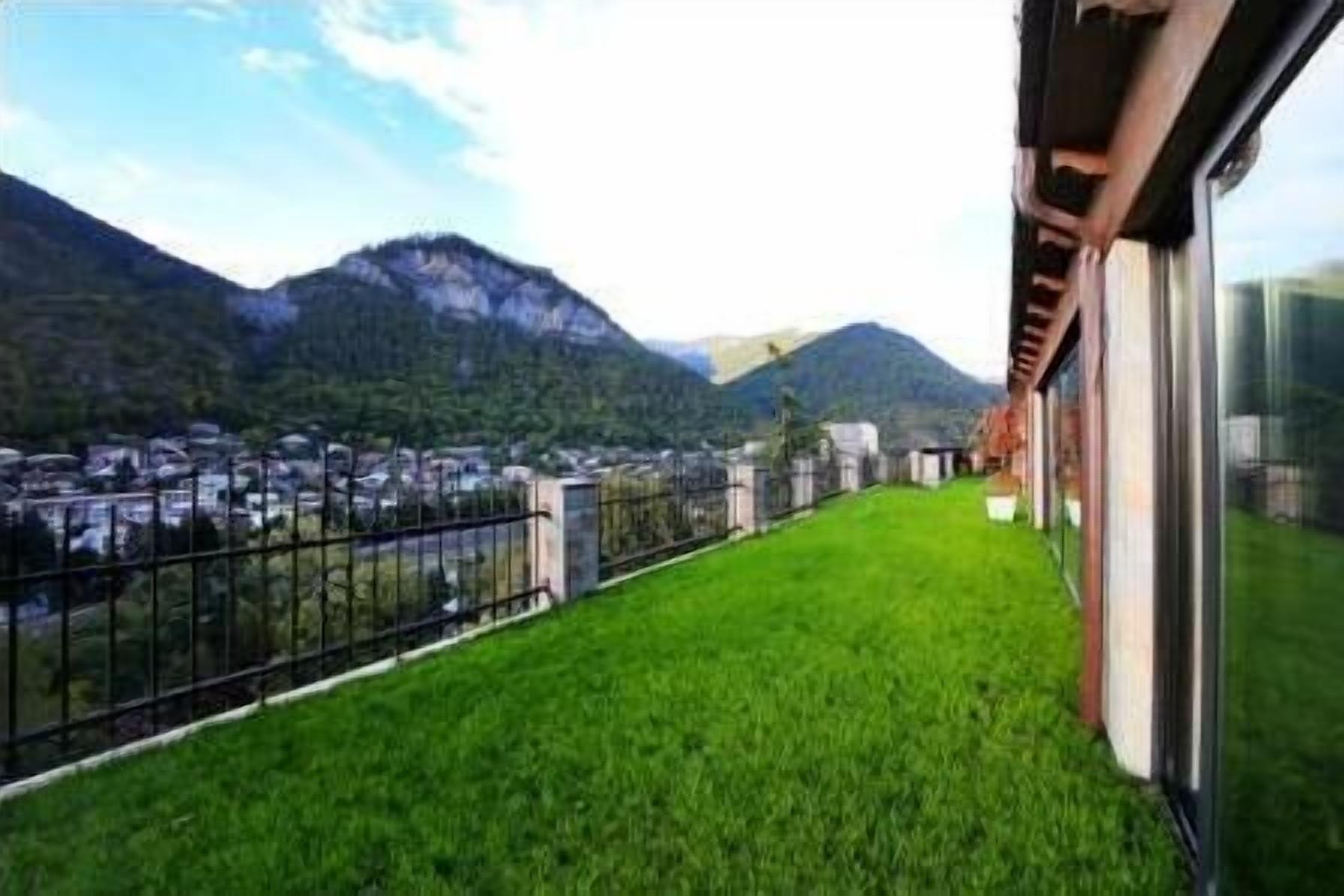 A balcony with a grassy area, a metal railing, and a view of a town and mountains in the background.
