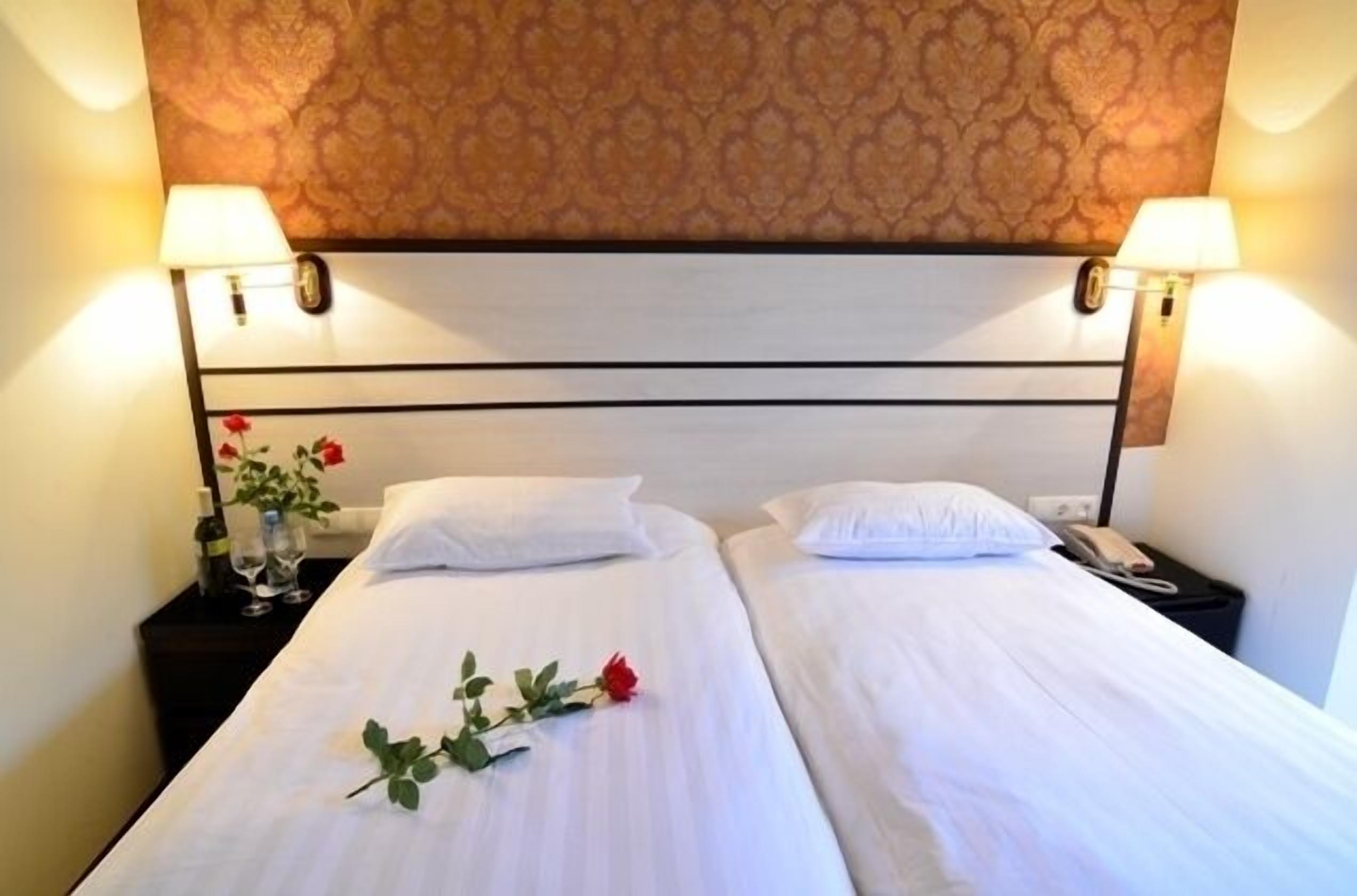 A double bed with white linens, two bedside tables with lamps, and a decorative wall pattern.