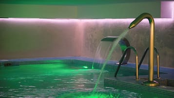 A spa area with a pool, green lighting, and a water feature.