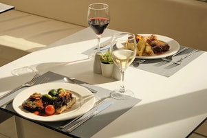 Una mesa servida con dos platos de comida, dos copas de vino y cubiertos.