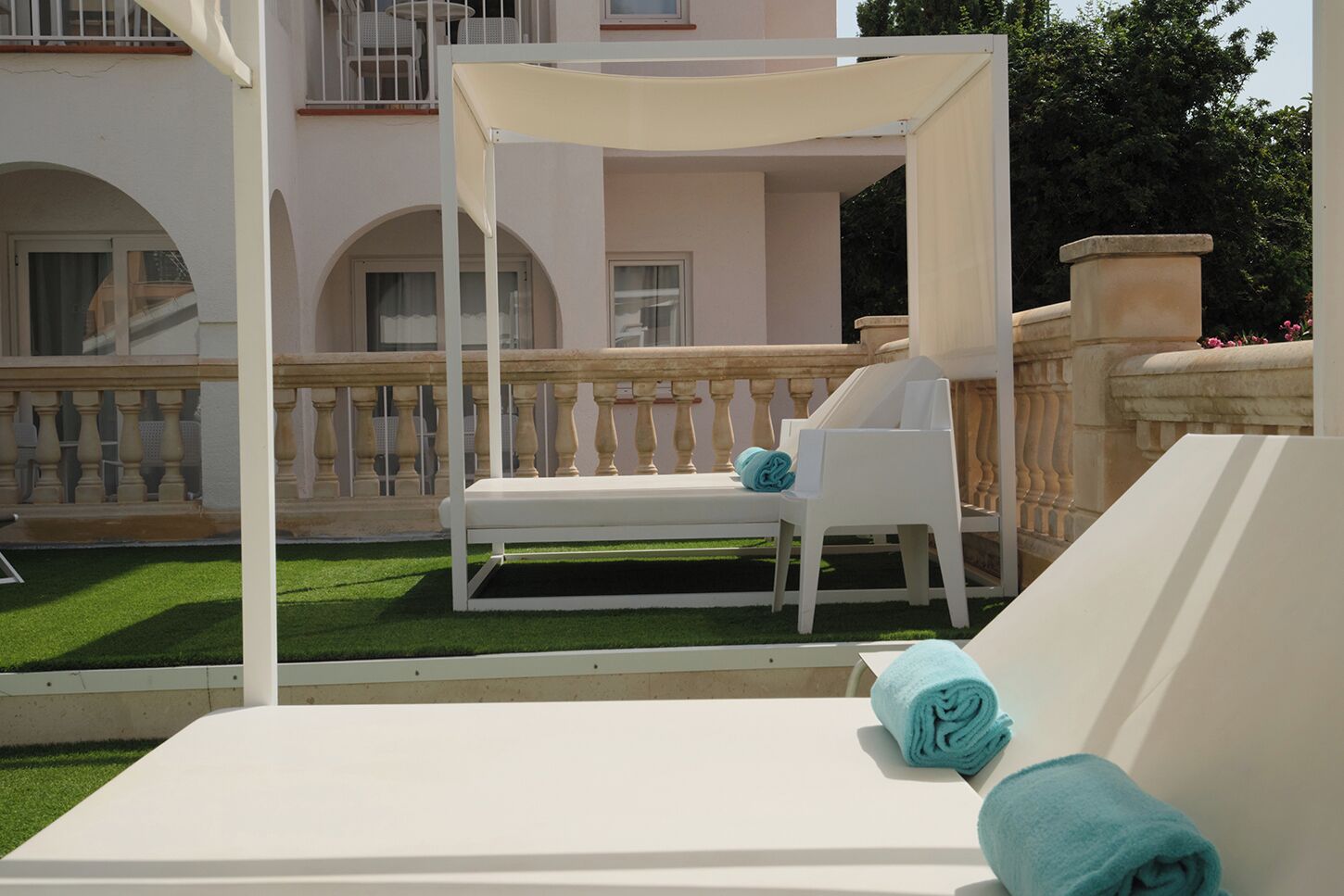 Een wit beschut terras met een loungesetje en een klein tafeltje.