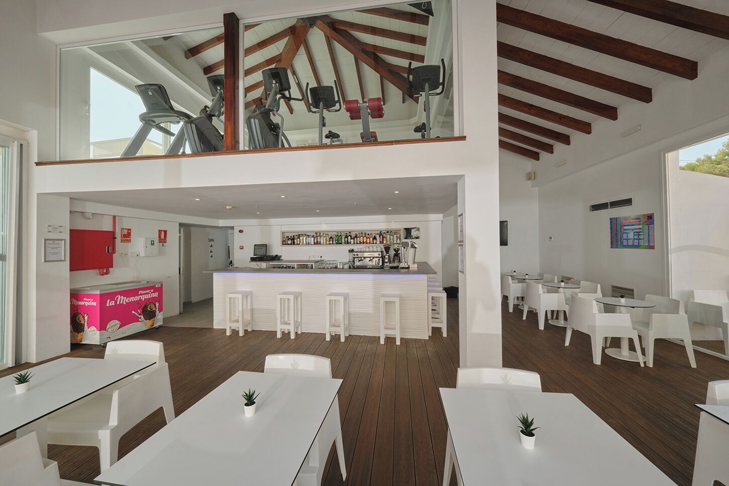 Un moderno vestíbulo de hotel con zona de bar, asientos y equipo de ejercicio.