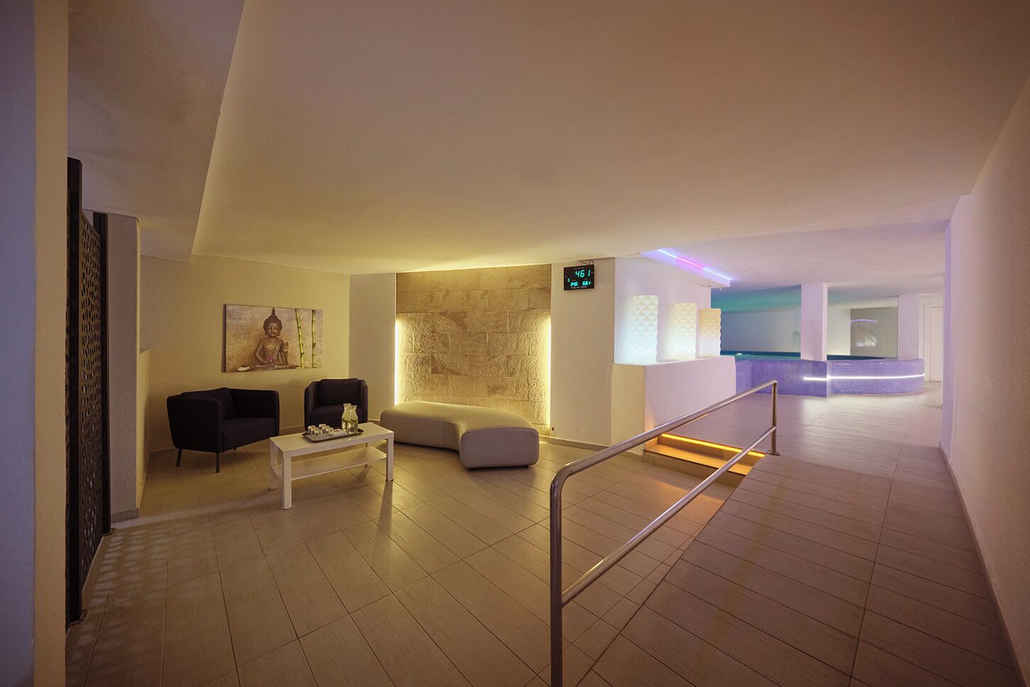 Un moderno vestíbulo de hotel con recepción, zona de estar y una escalera que conduce a otro nivel.