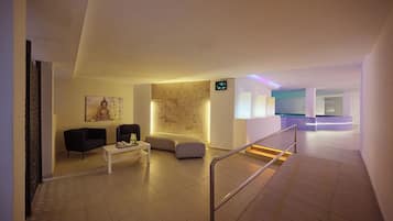 Un moderno vestíbulo de hotel con recepción, zona de estar y una escalera que conduce a otro nivel.