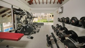 Un gimnasio con cintas de correr, una banca y un estante con mancuernas.