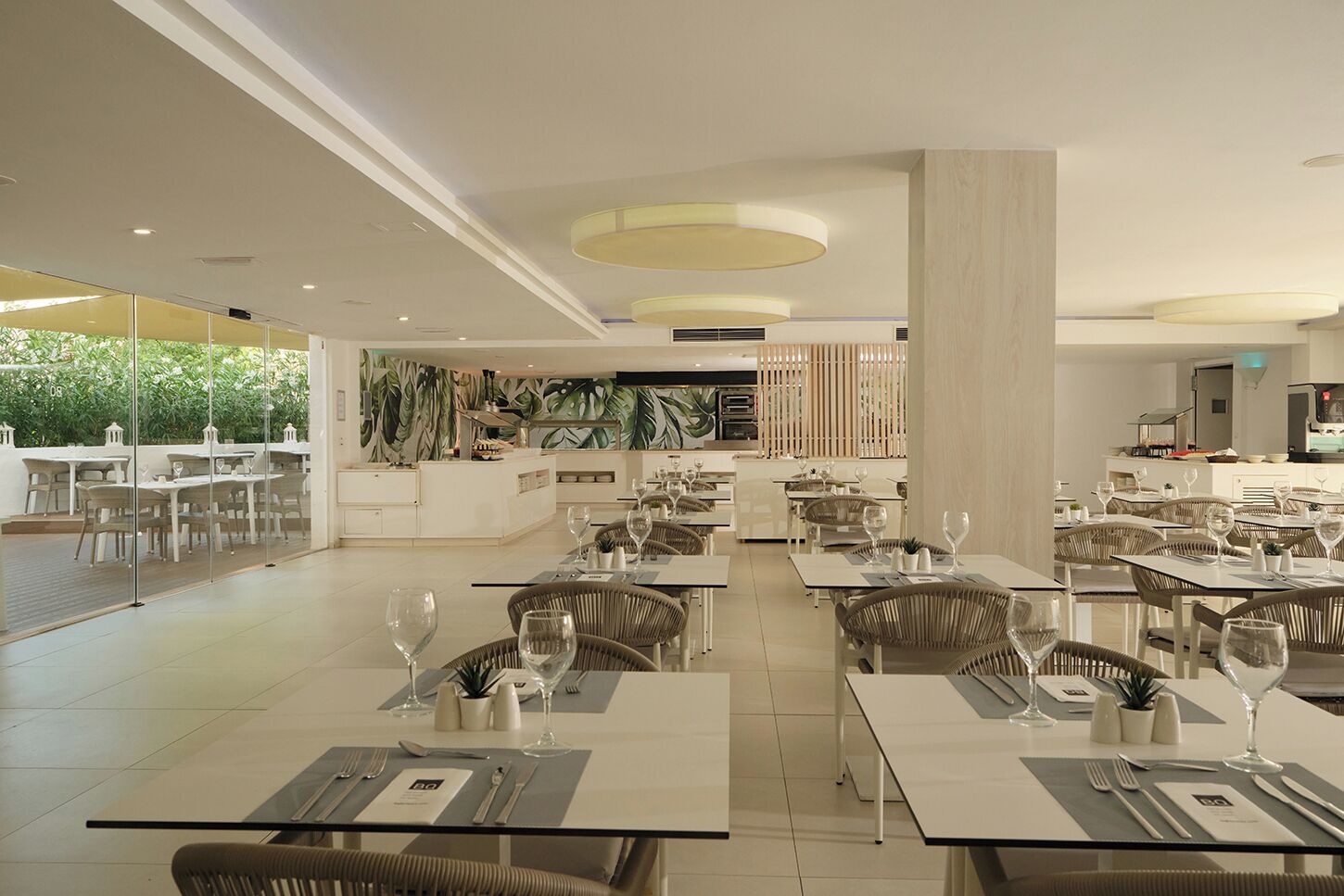 A spacious restaurant with high tables and chairs, a central island, and a view of greenery outside.