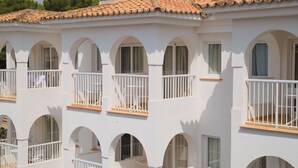 Un edificio de varios pisos con paredes blancas, múltiples balcones con barandillas blancas y un tejado de tejas.