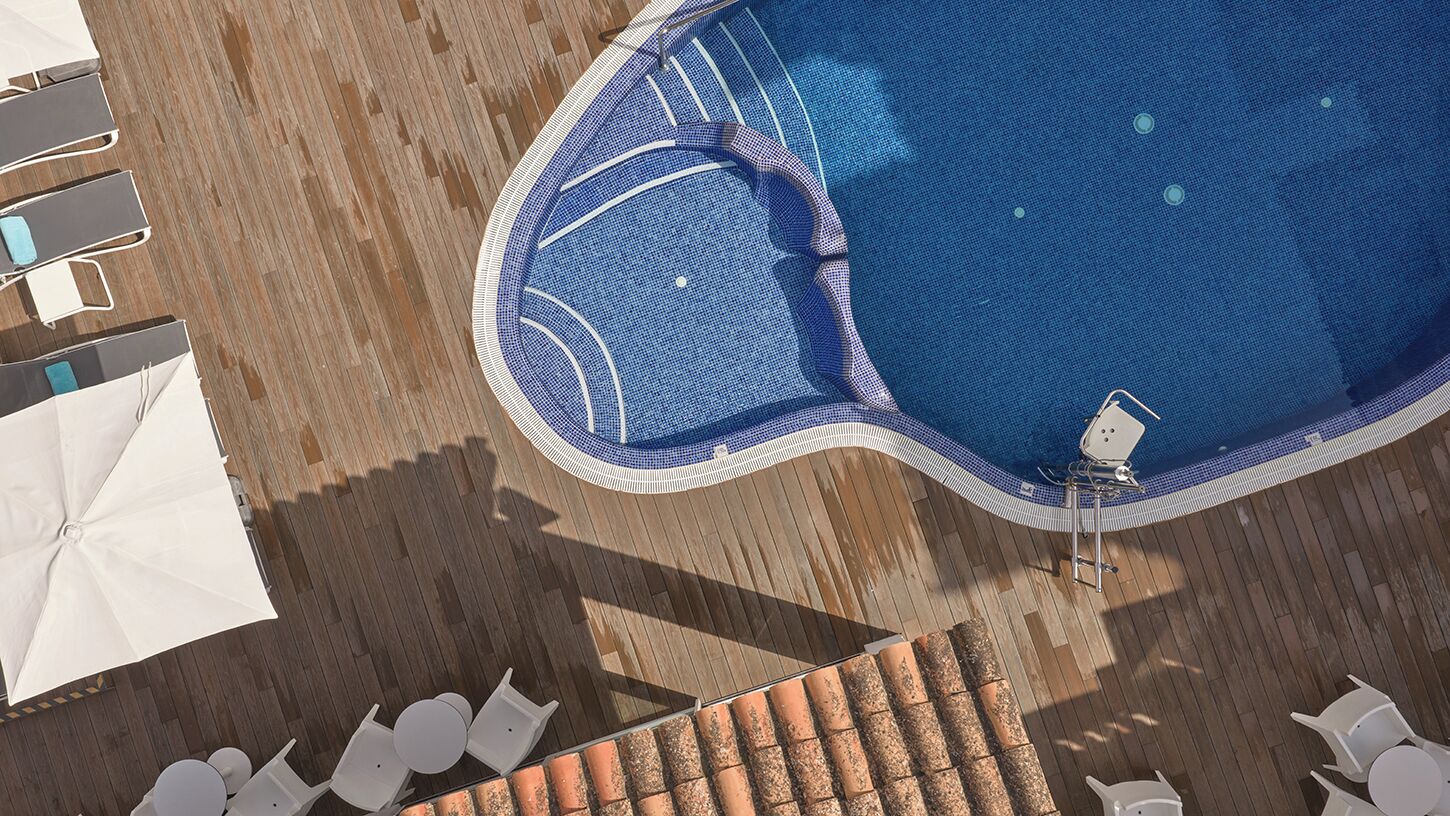 Vista aérea de uma piscina com borda azulejada, cercada por espreguiçadeiras e guarda-sóis.