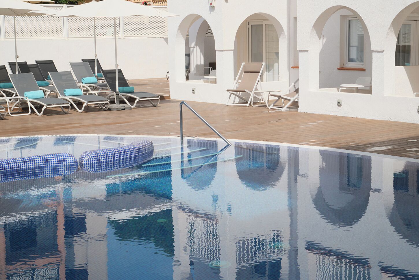 Una piscina con lettini e ombrelloni, circondata da pareti bianche ad arco.