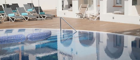 Una piscina con sillas de descanso y sombrillas, rodeada de muros blancos con arcos.