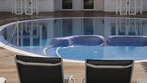 Una piscina con borde de azulejos, rodeada de sillones de descanso.