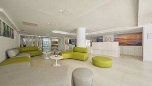 Un vestíbulo moderno con mostrador de recepción, zonas de estar en tonos verde y blanco y un mural grande en la pared.