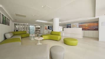 A modern lobby with a reception desk, green and white seating areas, and a large wall mural.