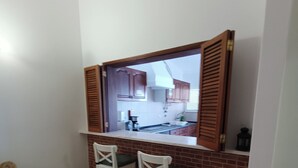 A compact kitchen with a brick backsplash, two white bar stools, and a window with wooden shutters. - Lagos Charming Villas (Lagos)