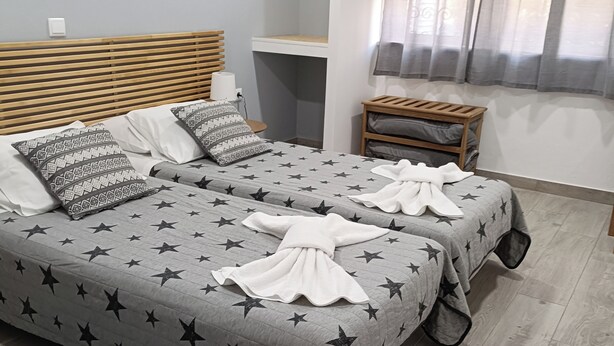 A hotel room with two beds, each with star-patterned bedding and pillows, a wooden headboard, a small wooden nightstand, and a blue rug. - Lagos Charming Villas (Lagos)