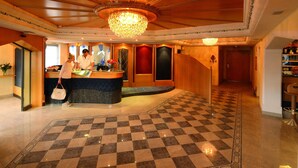 A lobby with a checkered floor, a reception desk, and a chandelier. - Sonnenhotel Adler (Villandro)