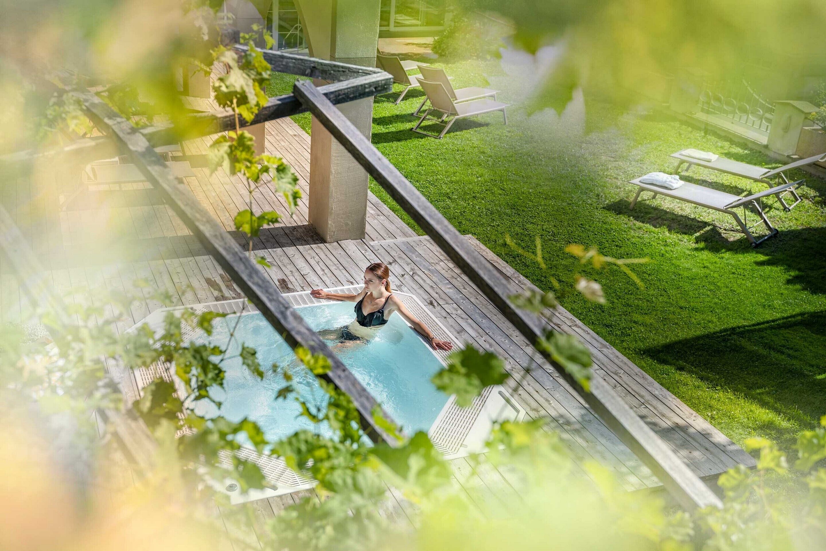 Eine Person im Swimmingpool, im Hintergrund eine Holzterrasse und Liegestühle.