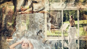 A person in a pool with a waterfall backdrop, a glass-enclosed area with a bench, and a person standing by the pool. - Sonnenhotel Adler (Villandro)