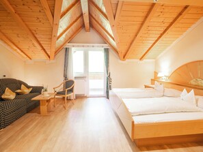 A room with a wooden ceiling, a sofa, a chair, a bed, and a small table. - Sonnenhotel Adler (Villandro)