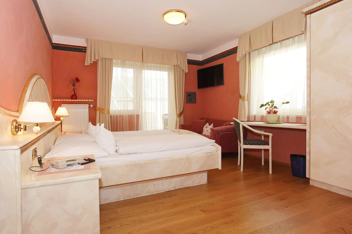A hotel room with a bed, bedside table, lamp, chair, desk, and a TV mounted on the wall.