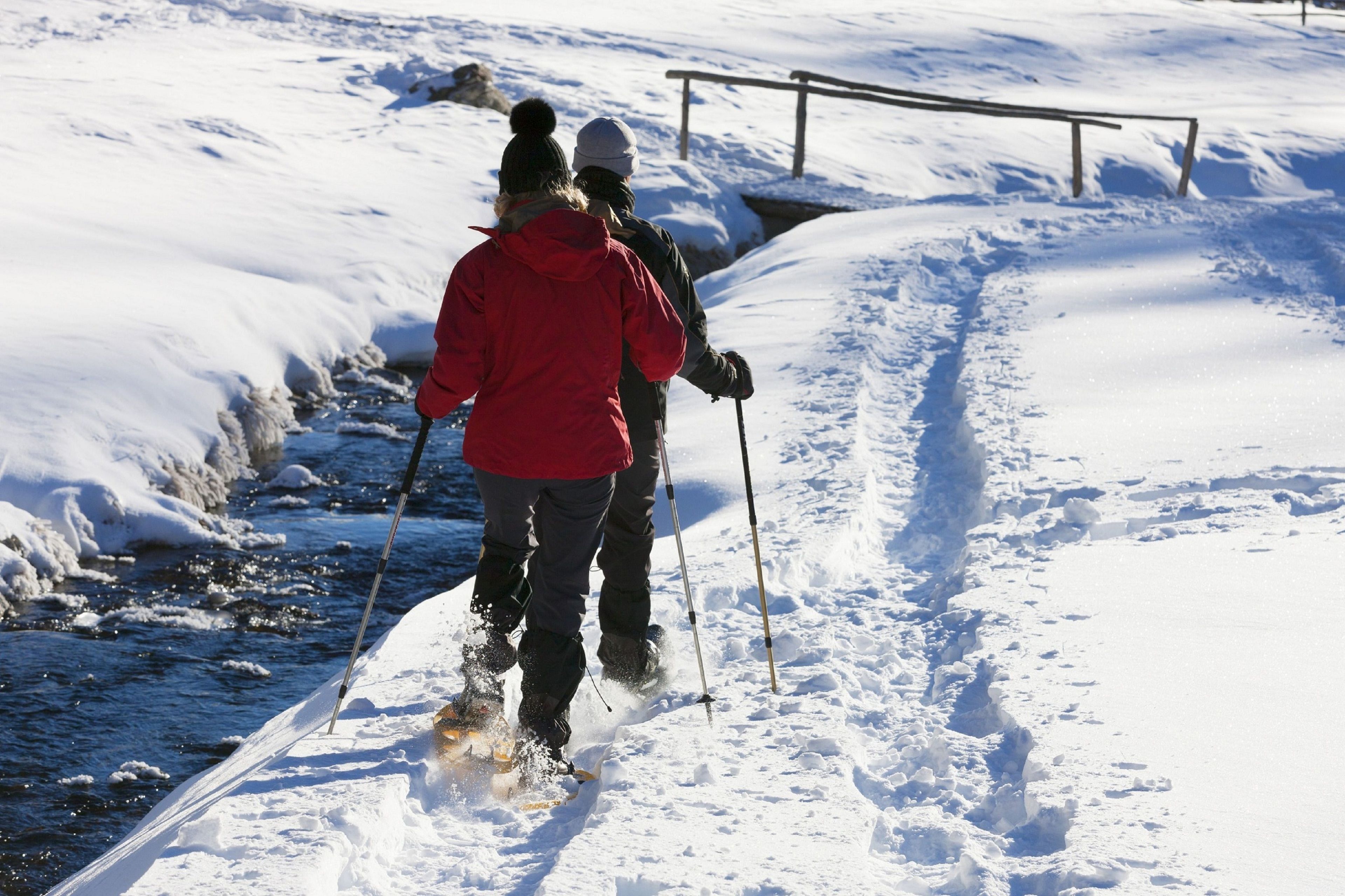 Deux personnes pratiquent le ski de fond sur un sentier enneigé, avec une rambarde métallique en arrière-plan.